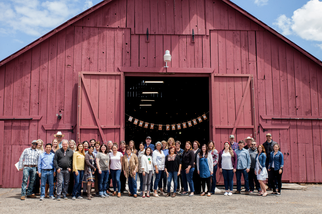 Group photo in front of a barn with ‘Howdy Partners’ sign